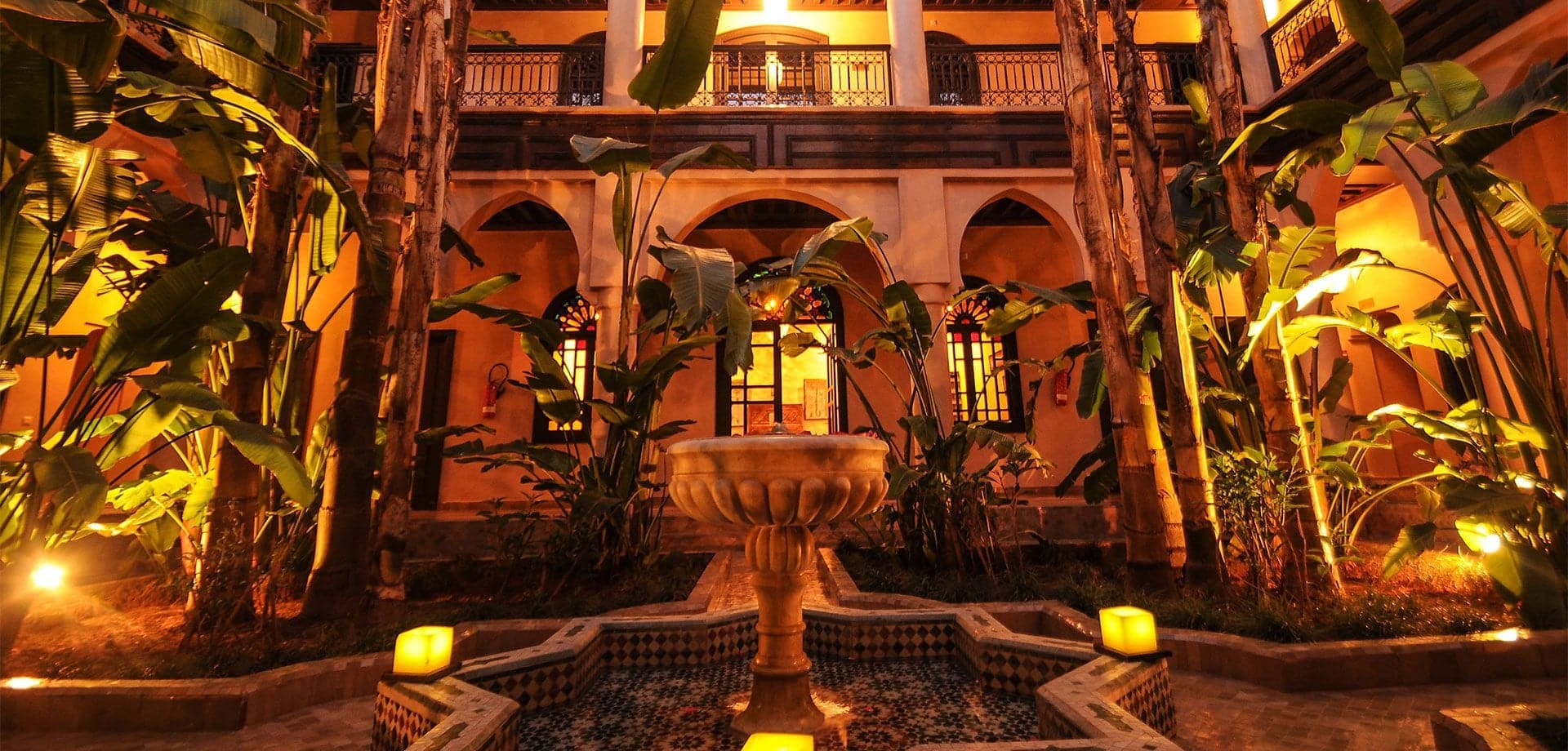 a fountain surrounded by a pink residence/house and plants and trees.