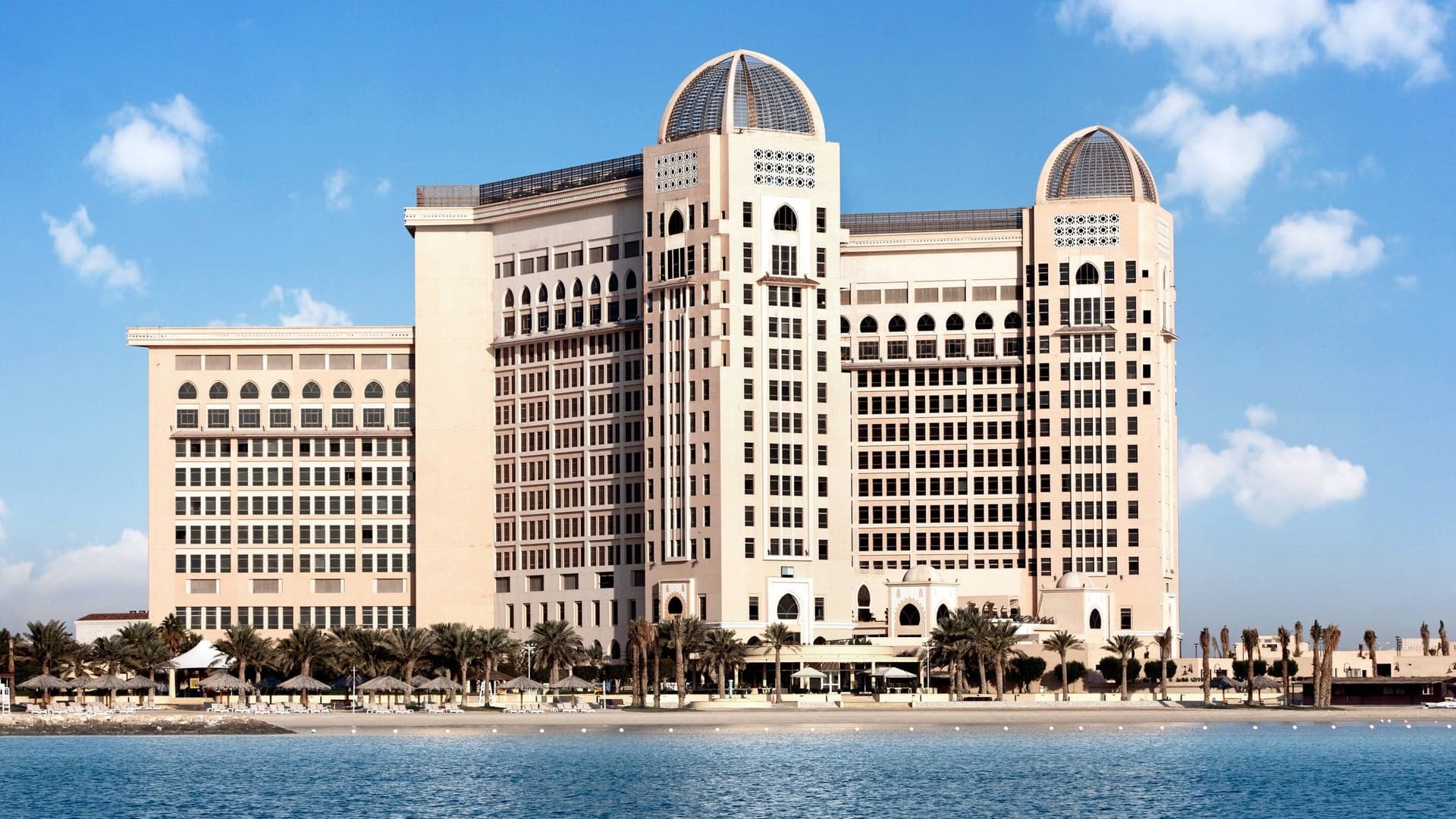 St Regis Doha, A outside perspective of the hotel, private beach and palm trees.