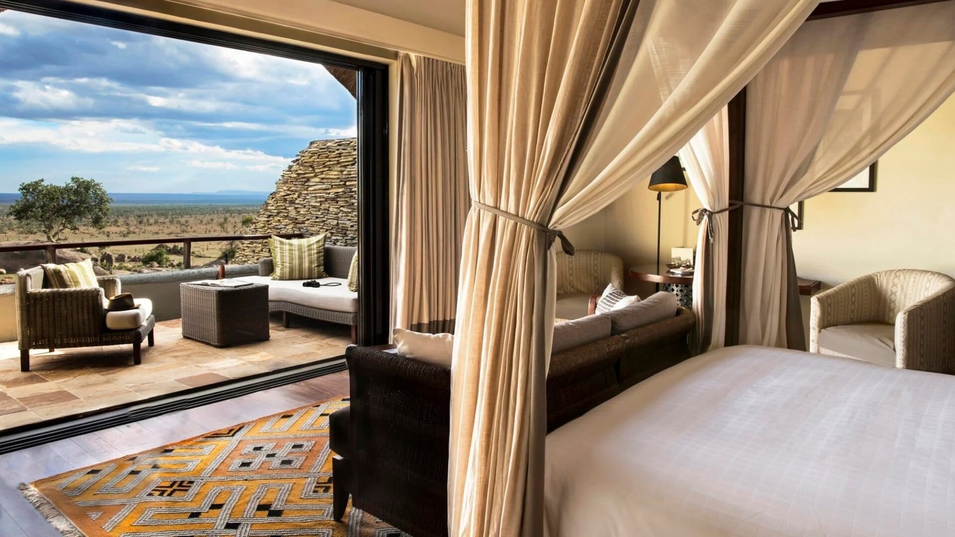 Suite with kingsize bed, couches, and a sofa leading to a private terrace with more sofas and couches and a view to the savannah. The suite has a cream coloured interior