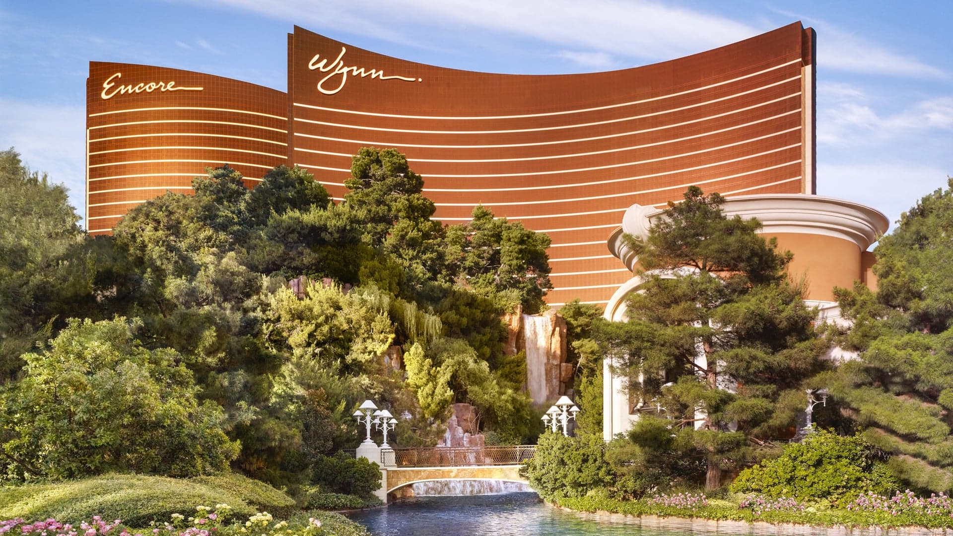 View of nature, gold and white bridge and the massive brown/bronze coloured building with white stripes saying: Encore and Wynn.