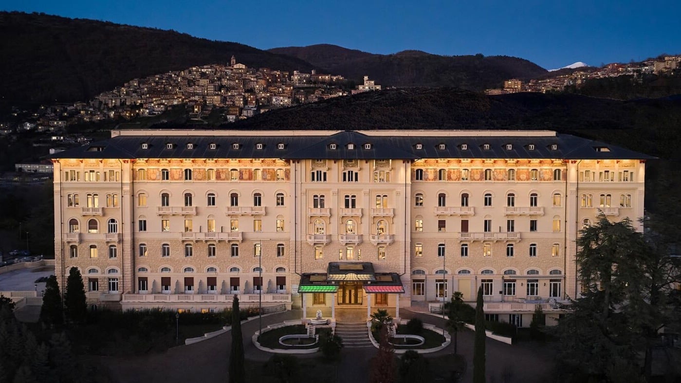A large white stoned hotel with a entrance with green and red lights.