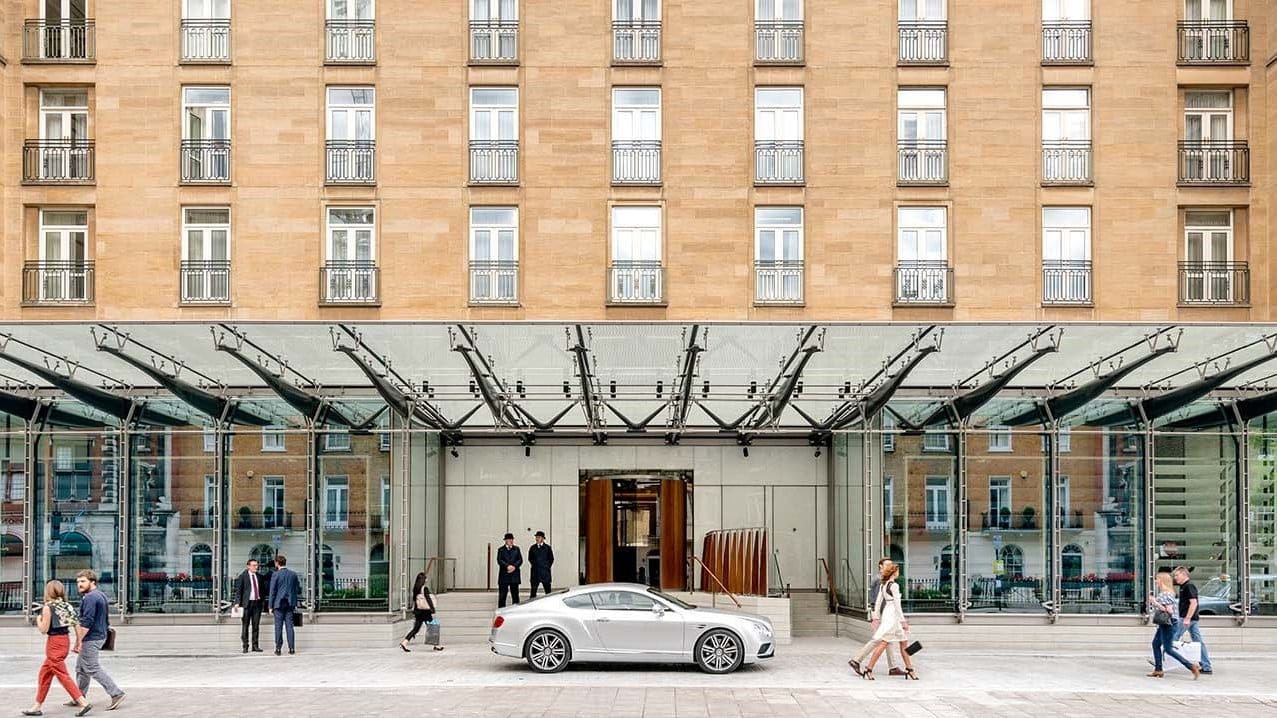 Front entrance of the berkley london with two doormen and a grey car infront.
