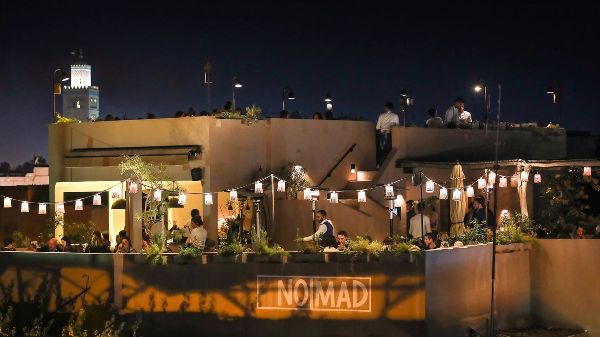 a white stone resturant with two levels with people. Nomad written in white in front.