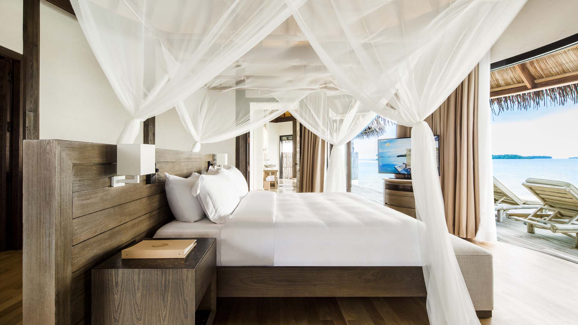 White kingsize bed, wooden decor, flatscreen tv, entrance out to the water and sunbeds.