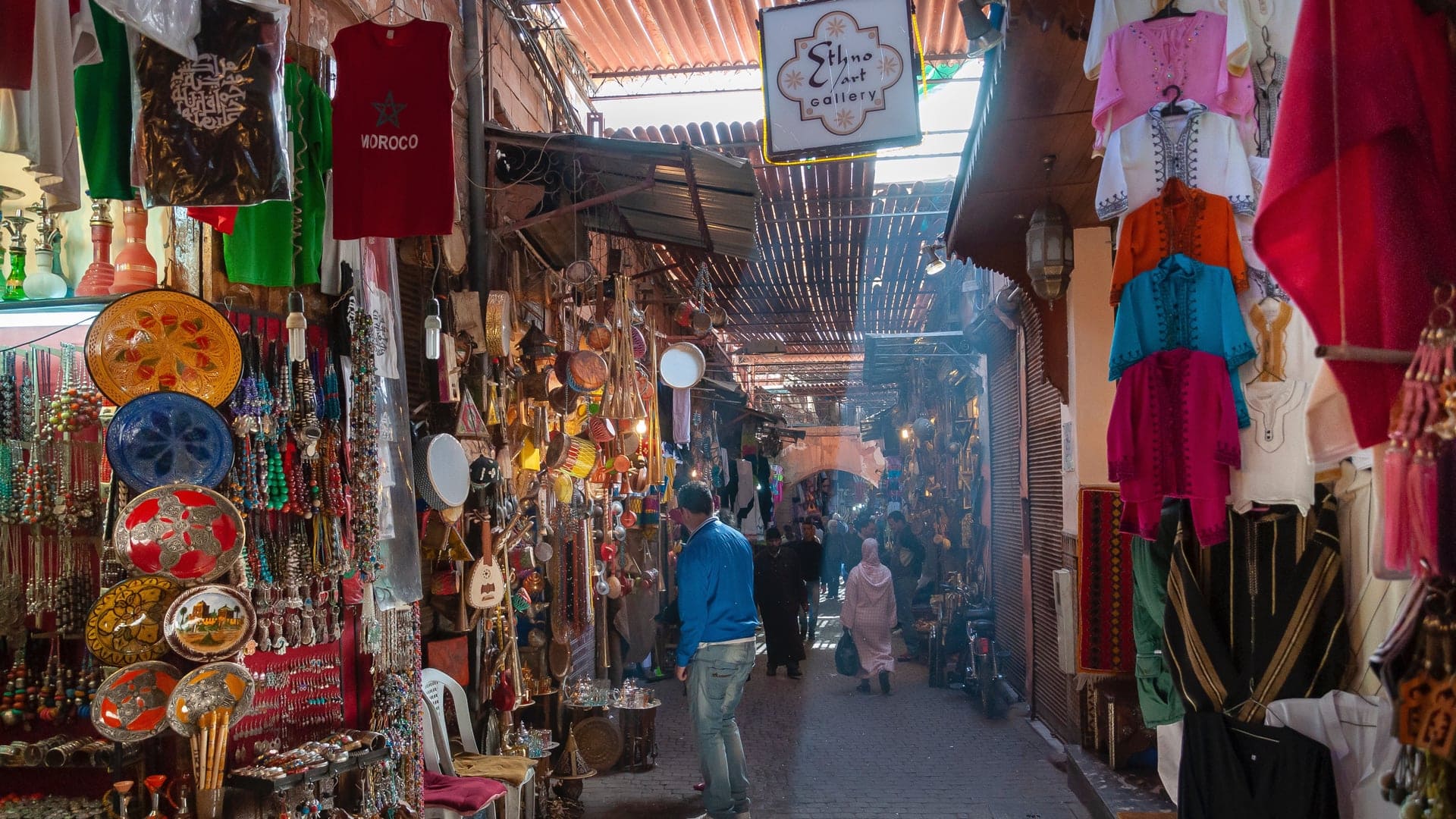 Moroccan market with people walking between. Man in blue jacket.