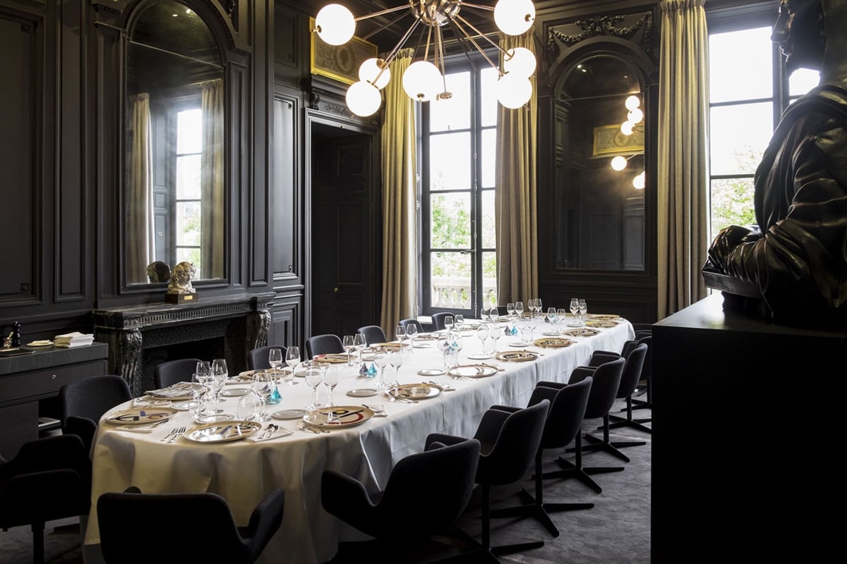 Big oval table with black chairs and black walls at guy savoy paris