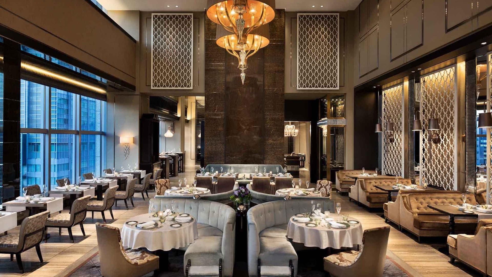 Dining area with grey decor sofas and beige design chairs, marble walls, large golden lamp and windows to the city.