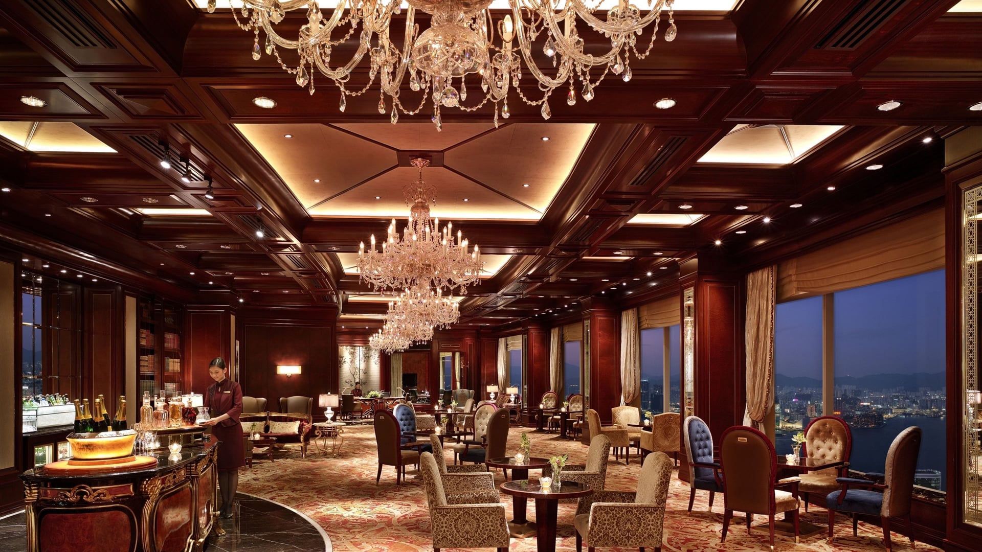 Bar area at Island Shangri-La in Hong Kong, with a woman in red preparing drinks and multiple windows and seating areas.