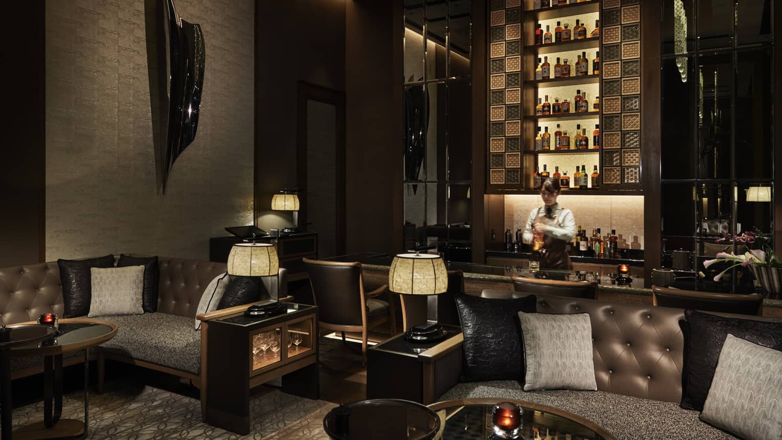 Bar Virty with dark coloured furniture, black wall art/sculpture and woman in uniform making drinks.