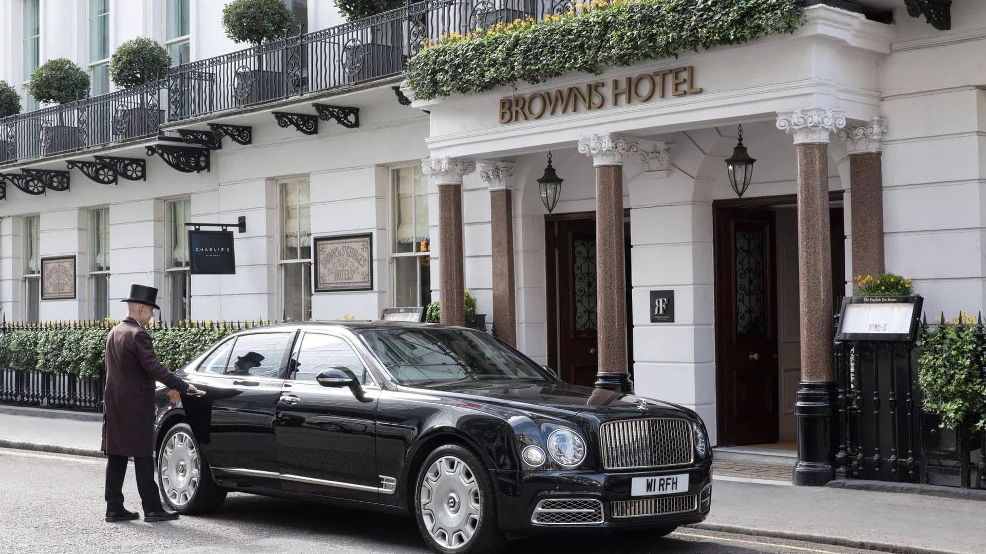 Front entrance of browns hotel london with a doormen opening the door of a black bentley.