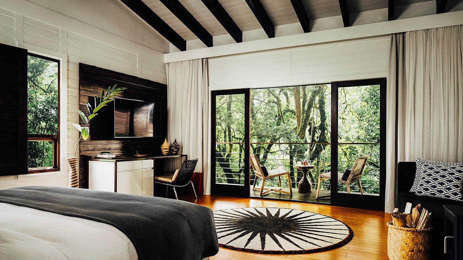 Suite with white and black furniture, wooden floor and a terrace with a jungle like view