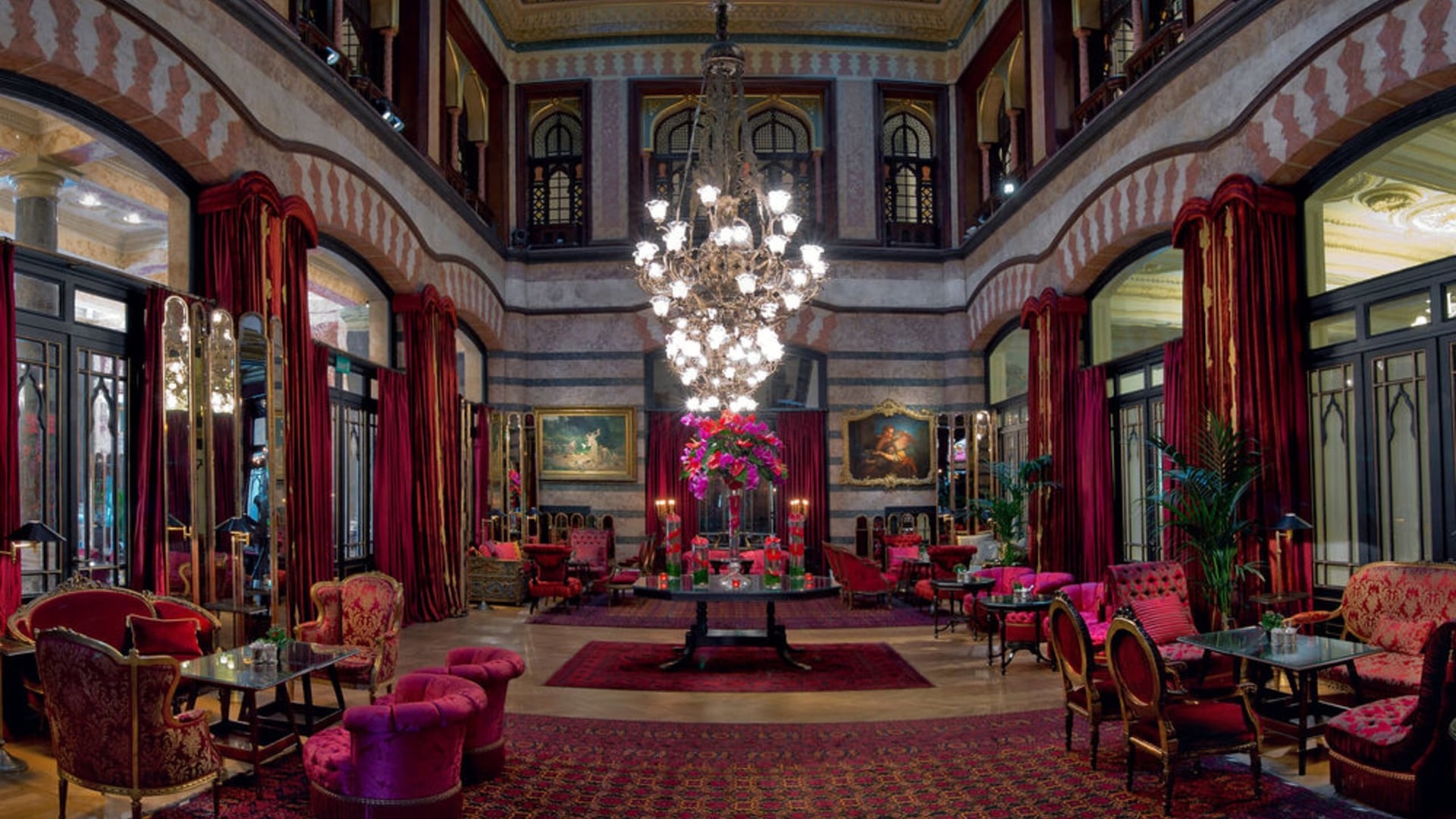 Large and vibrant lounge at The Historic Pera Palace, offering vibrant red/pink colours and a large lamp to set the mood for a romantic setting