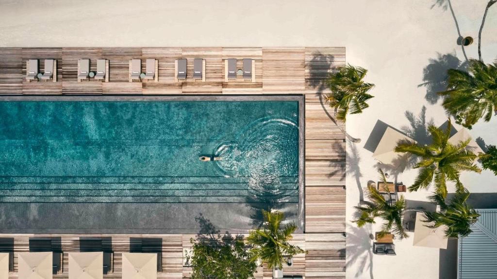 Bird view of pool area in Patina Maldives, Fari Islands with palmtrees, and man swimming in pool.