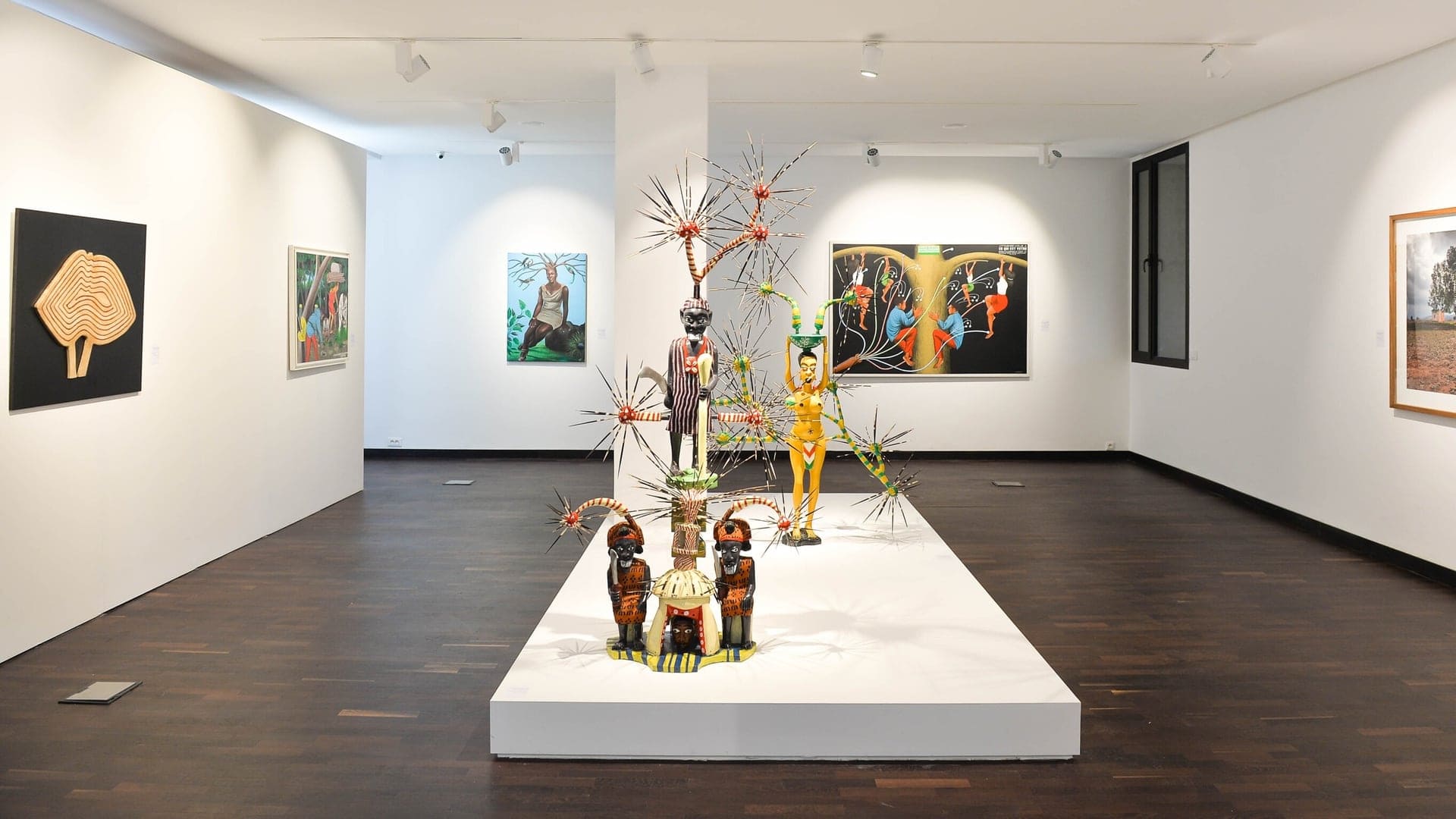 Original artwork done by young africans. A brown wooder floor with white walls and roof. Paintings hanging on the walls.