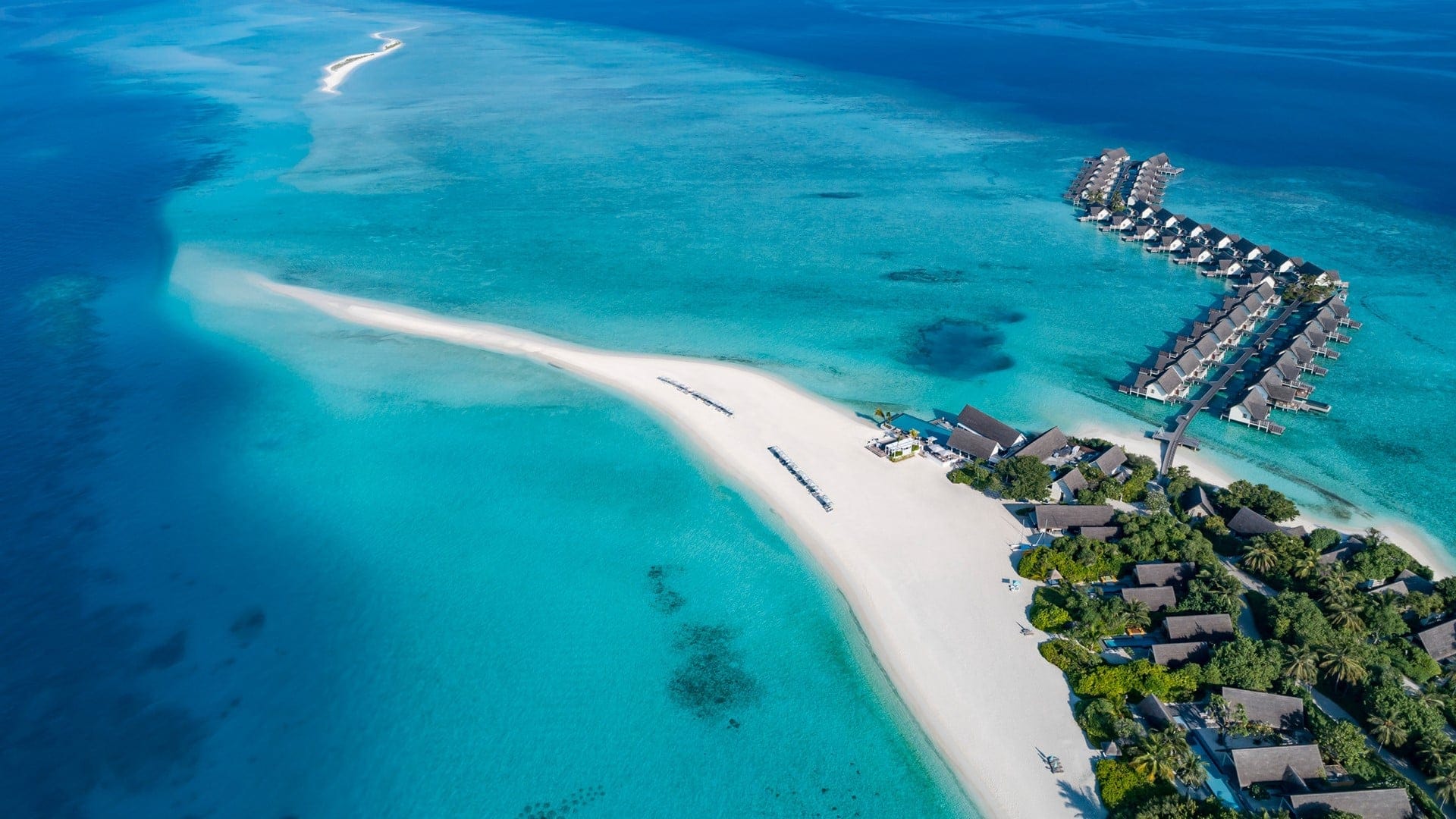 Bird perspective of the Four Seasons Resort Maldives at Landaa Giraavaru. Large island with cabin extensions to the water with palmtrees and crystal clear water.