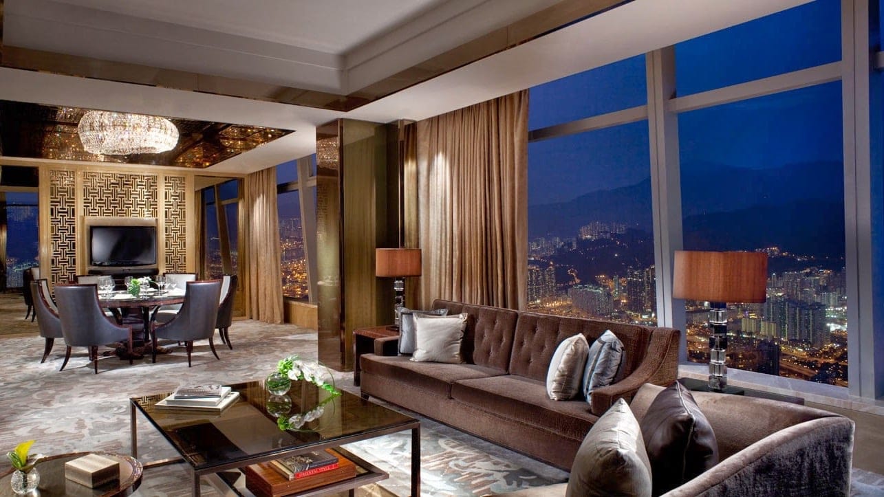 Suite at The Ritz-Carlton Hong Kong, large windows, dark brown sofas, dining area, with luxerious gold decor.