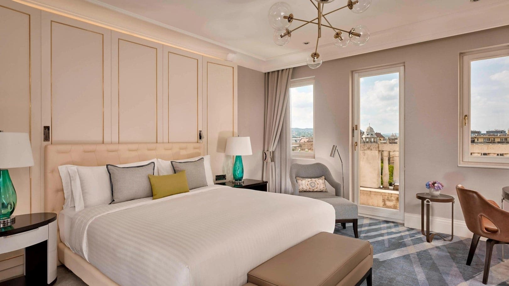 hotel room at The Ritz-Carlton in Budapest with white kingsize bed, windows, grey chairs and night lamps.