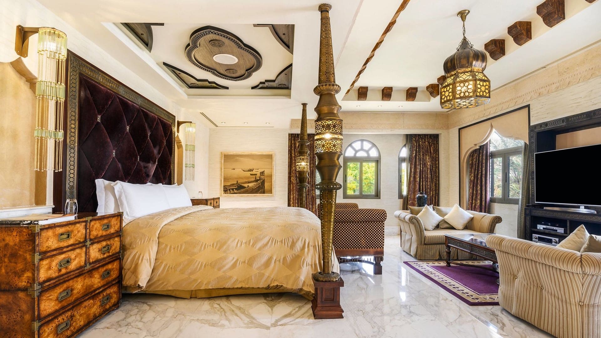 Hotel room in Sharq Village å spa - The Ritz-Carlton with authentic Arabian architecture, king size bed, lounge with large tv, bedside table and large windows.