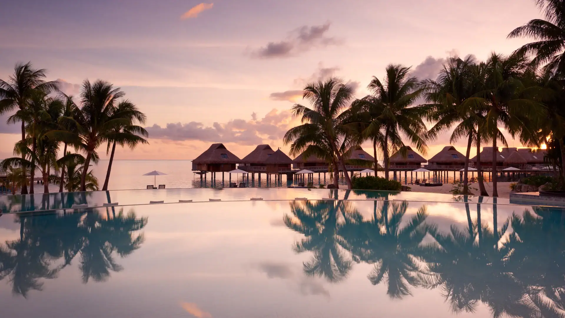 Infinity pool, view of the ocean, palm trees, and wood cabins in Conrad Bora Bora Nui