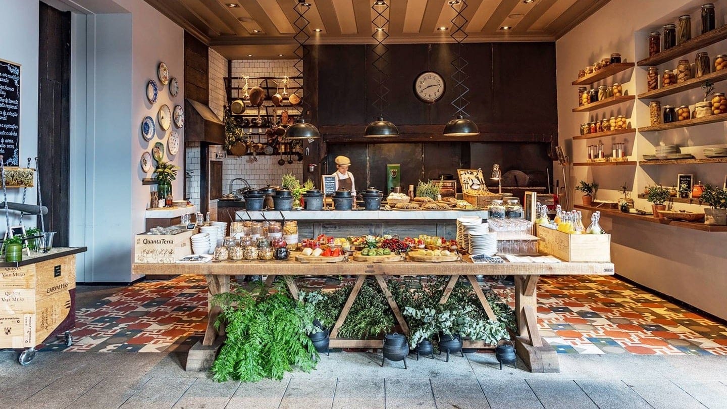A small buffet with different foods, fruit and drinks. A man worker standing behind.