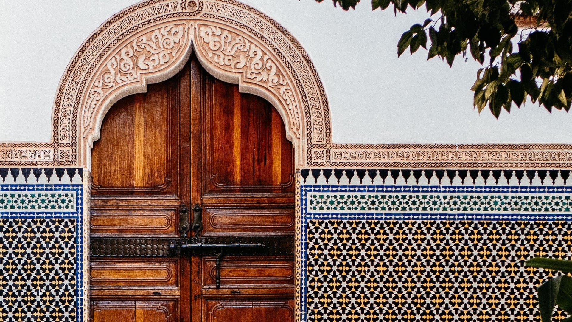 A large wooden door with polished clay tiles walls making a pattern of yellow, blue, white, black and pink.