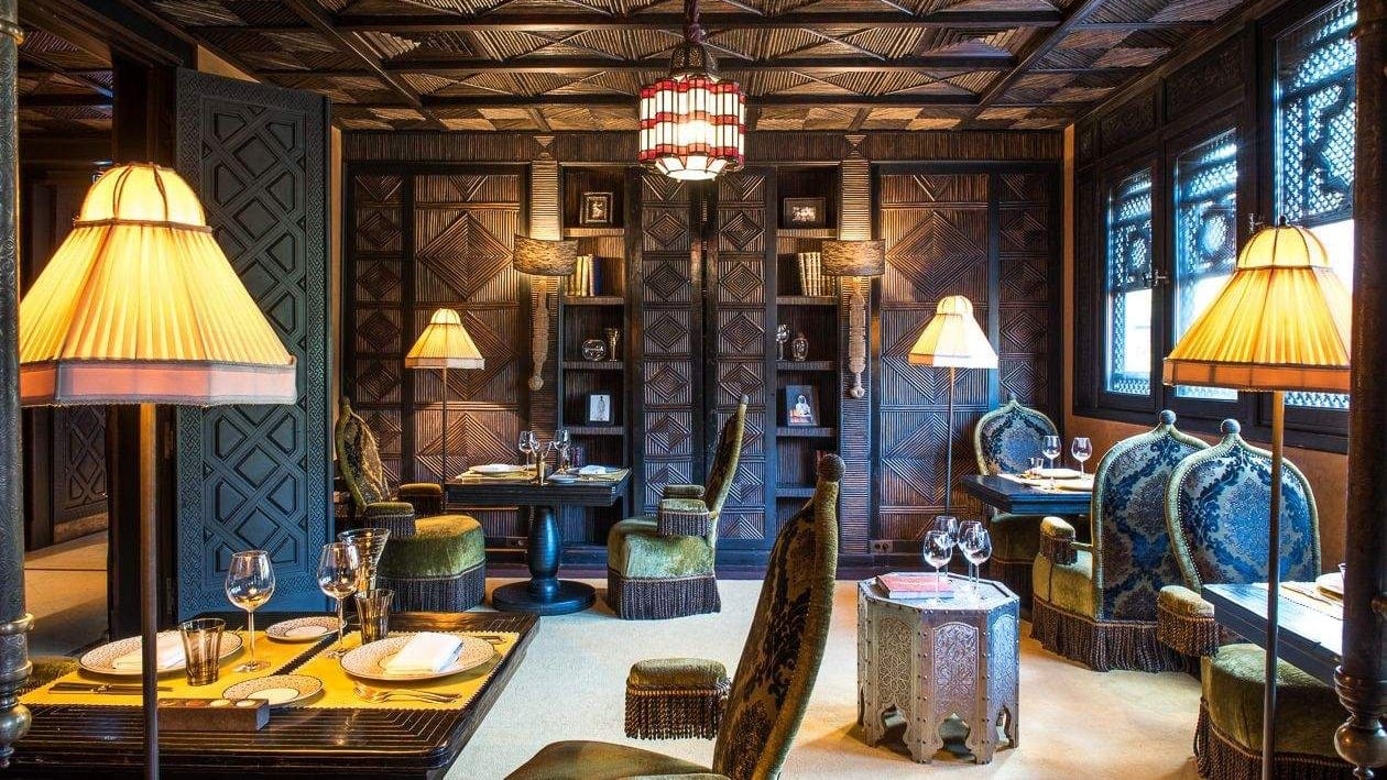 Indoor lounge with brown patterned ceiling and walls. A green patterned door. Green silk chairs and yellow lamps.