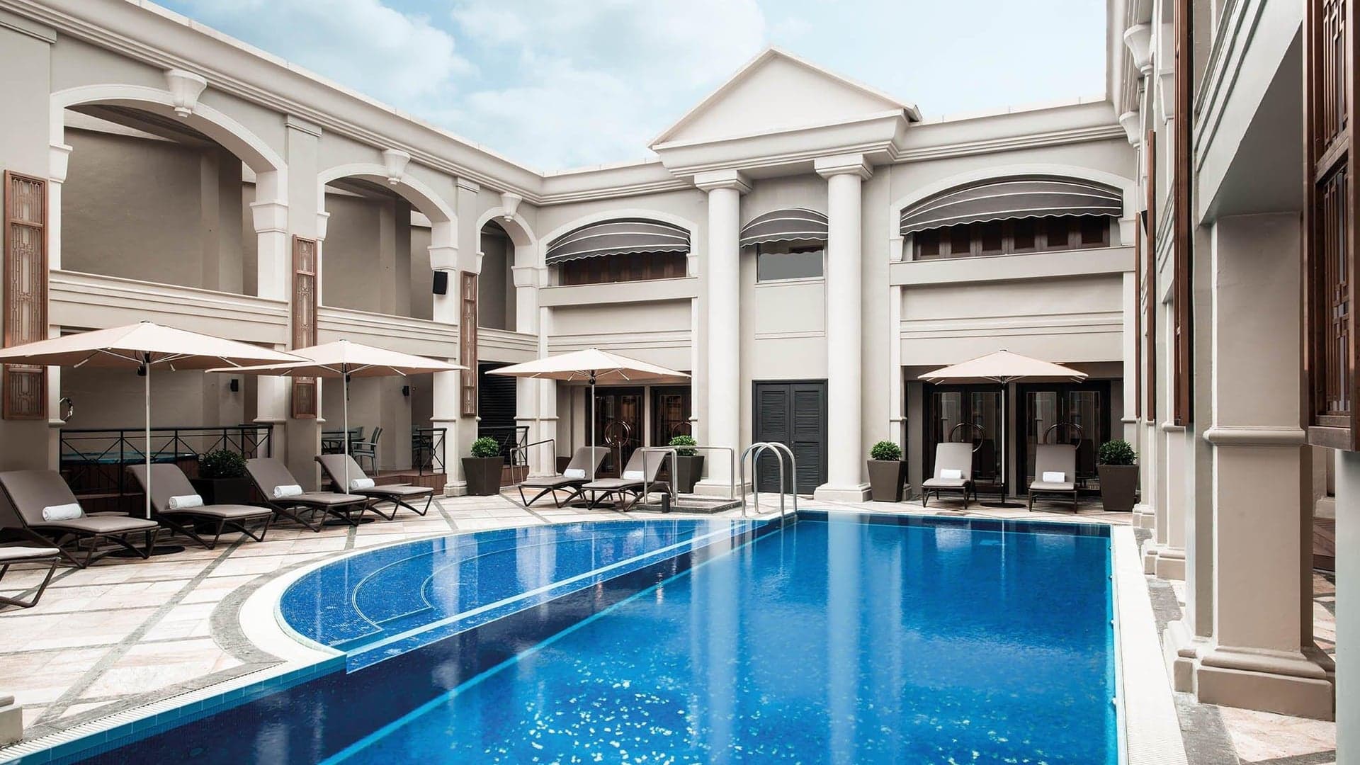 Pool area with white decor and white building surrounding it with sunbeds at The Langham in Hong Kong.