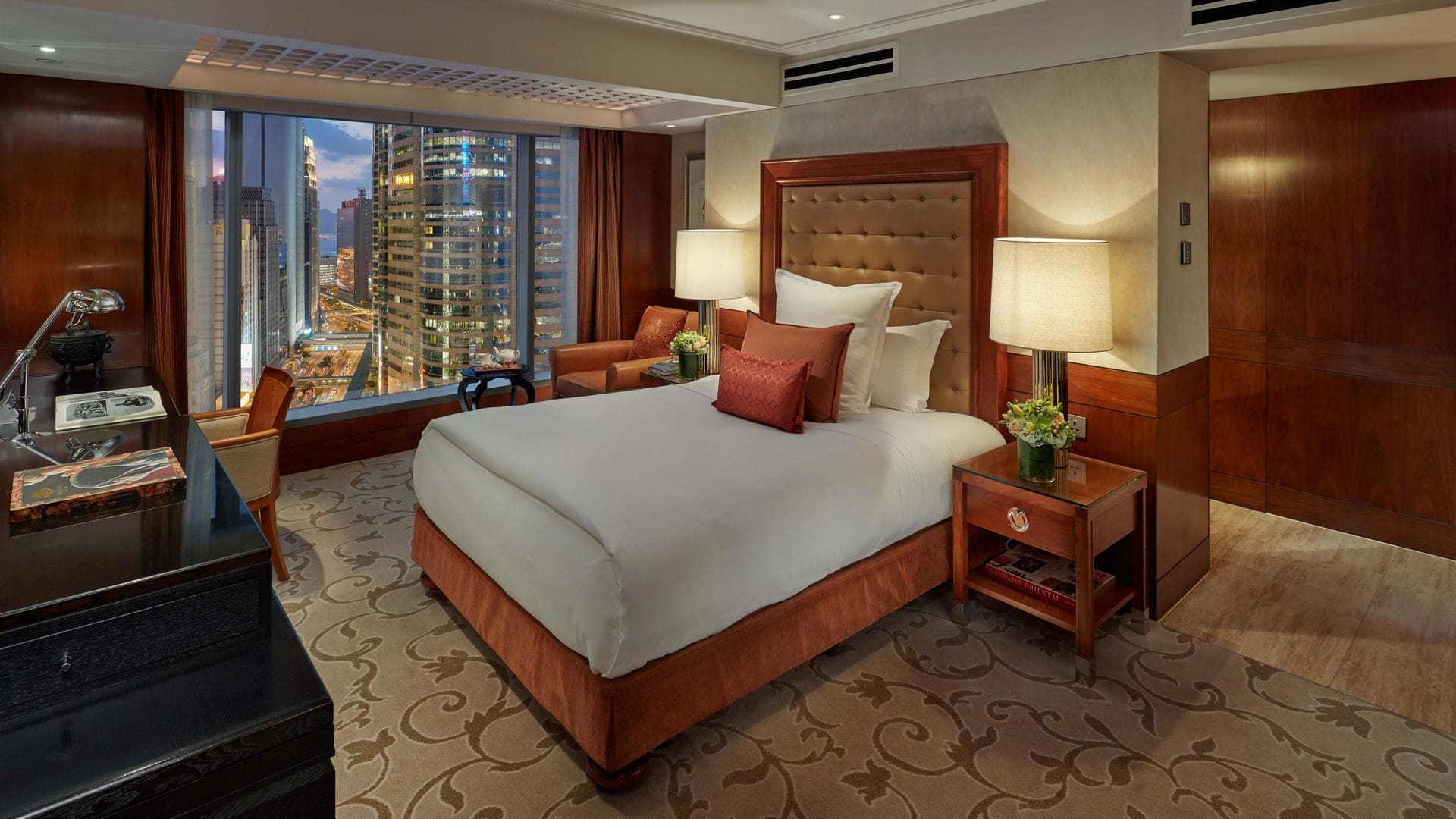 Hotel room featuring dark red wooden walls, patterned carpet, single bed, sofas, and work desk and view to Hong Kong at Mandarin Oriental Hong Kong