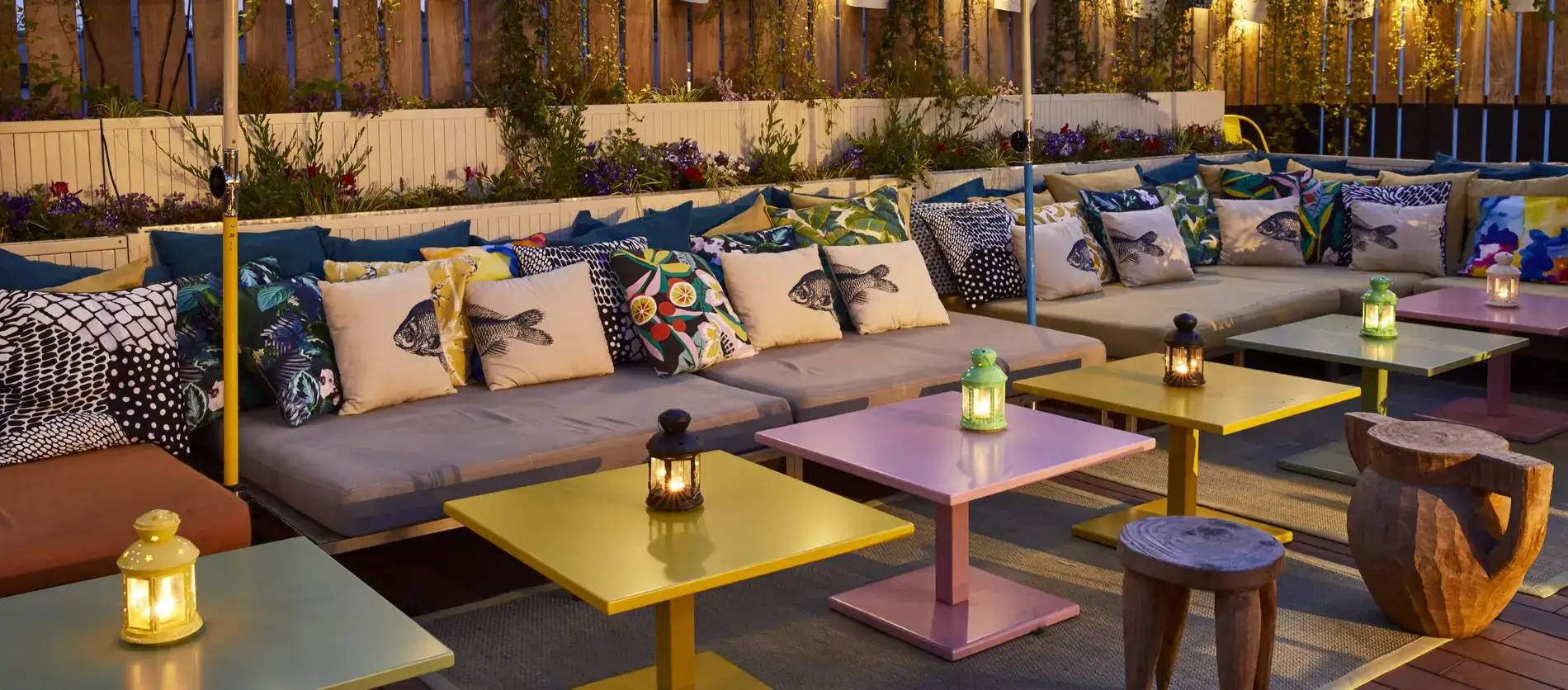 Colourful tables, grey sofas, fish pillows and tender lightning at Mama Shelter Paris East Rooftop.