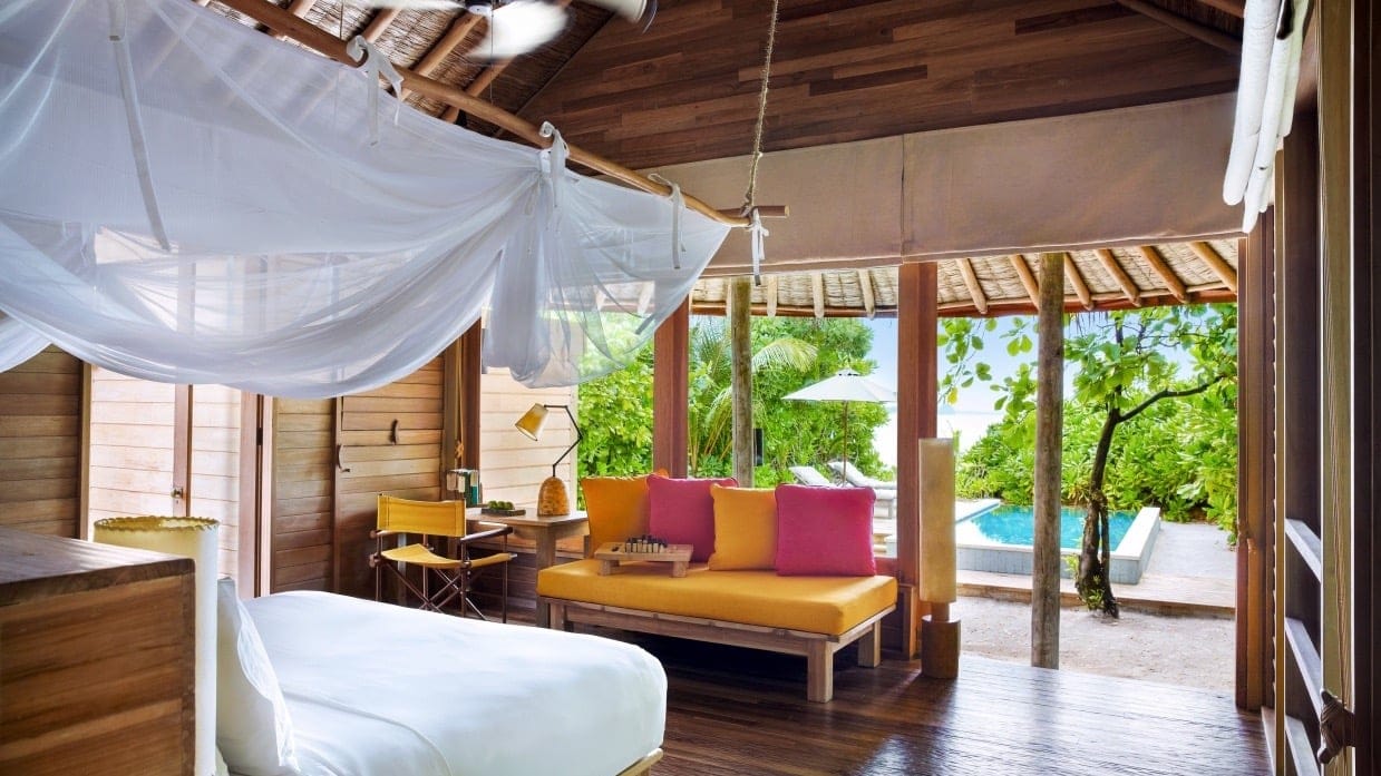 Suite at Six Senses Laamu with orange and pink sofa, kingsize bed, and private pool with sunbeds.