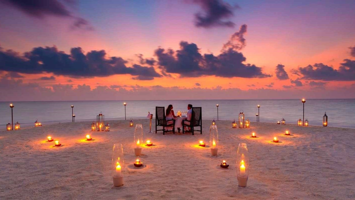 Couple eating on the beach with tender lighted lamps at Baros Maldives.