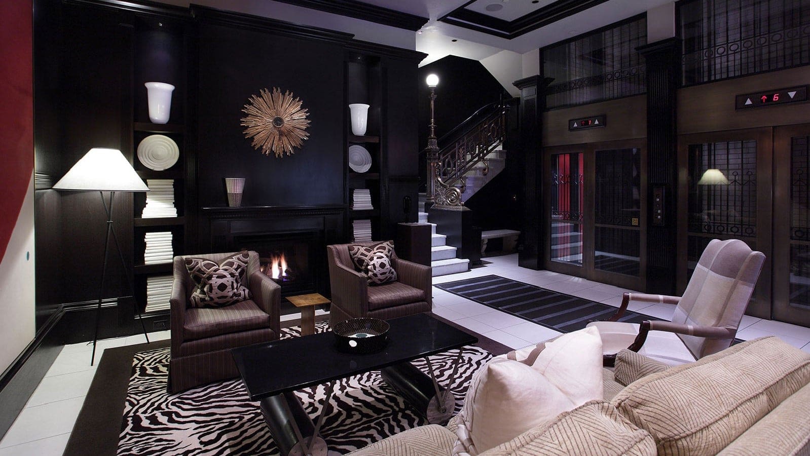 A seating area in the XV beacon with brown and white furniture, a black fireplace and a double elevator on the right.
