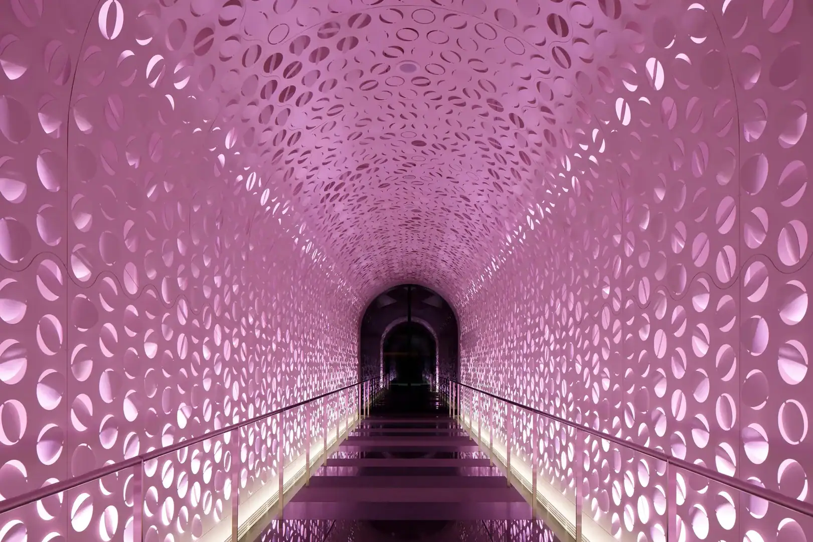 Corridor with pink lighting as walls and roof and a  black walkway 