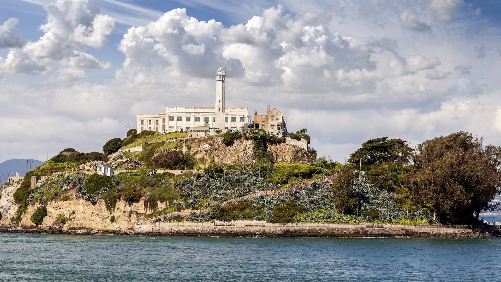 View of the Alcatraz, a large white building on a island with green trees, this was discovered by Spanish man Juan Manuel de Ayala and Alcatraz was once a high security prison that held Americas most notorious gangsters.