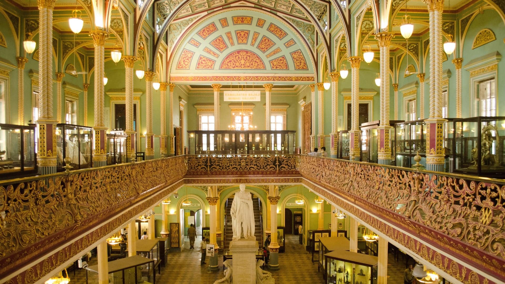 Inside a warm coloured museum with sculptures and green and red decor.