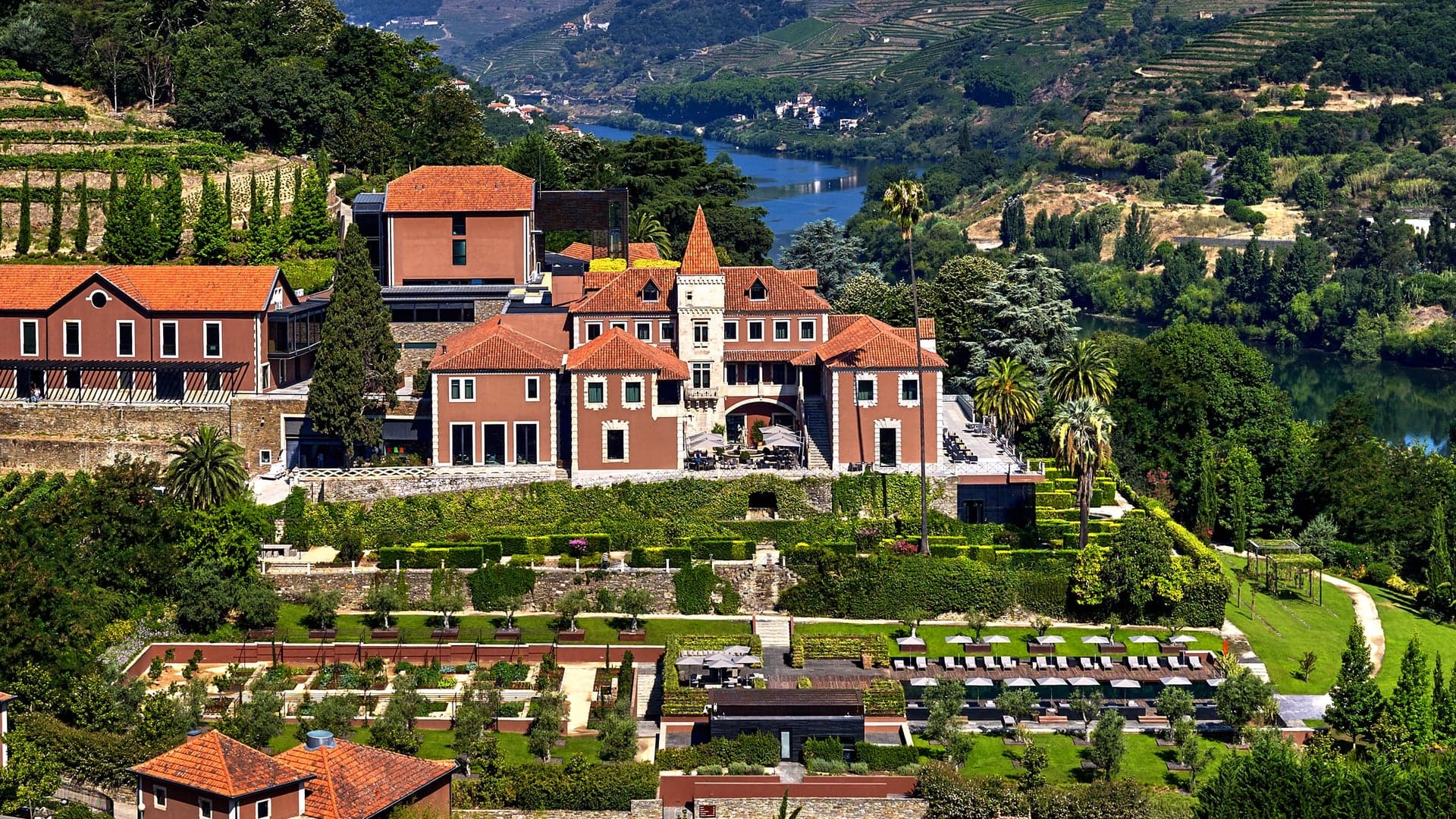 A hotel in a valley surrounded by a lake and a beautiful green garden