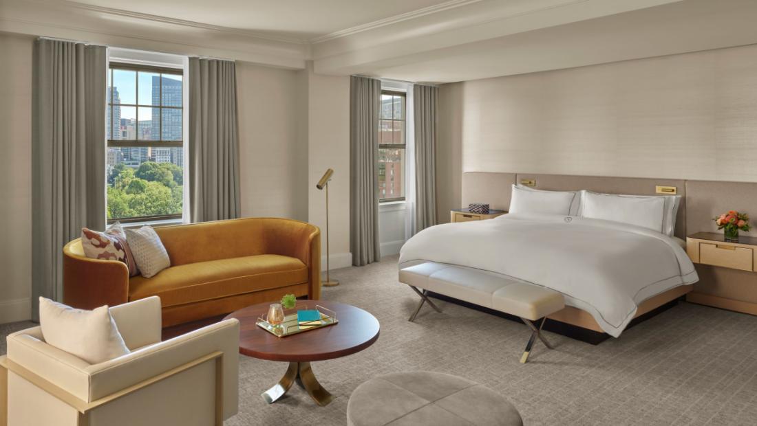 Hotel suite with a king sized bed, a yellow sofa, grey curtains and white walls,